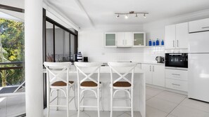 Une cuisine moderne avec des meubles blancs, un four noir et un coin repas avec des chaises blanches.