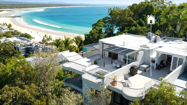 Una casa moderna con un patio en la azotea que da a una playa y al océano.
