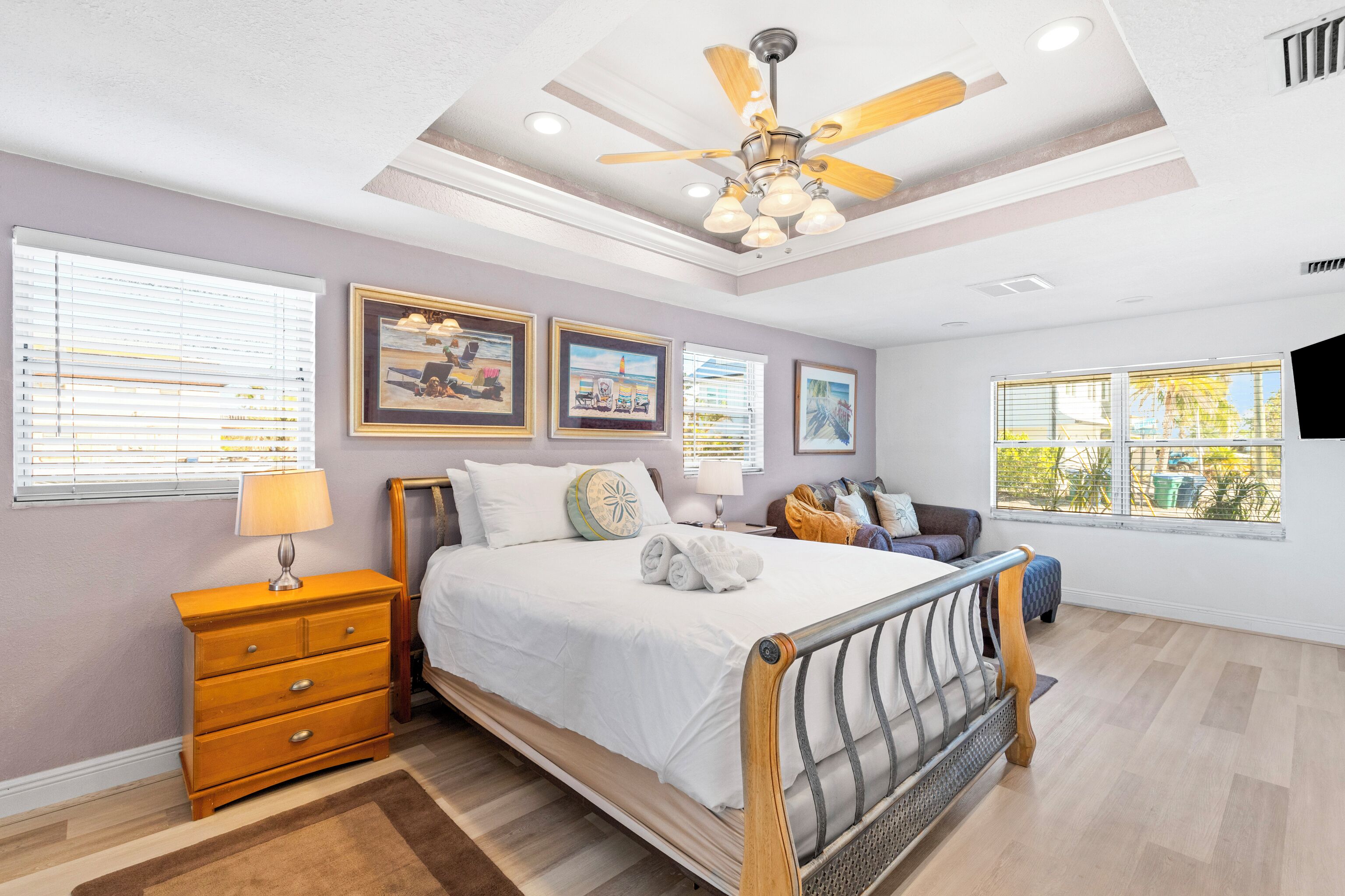 A bedroom with a bed, wooden dresser, ceiling fan, and artwork on the walls.