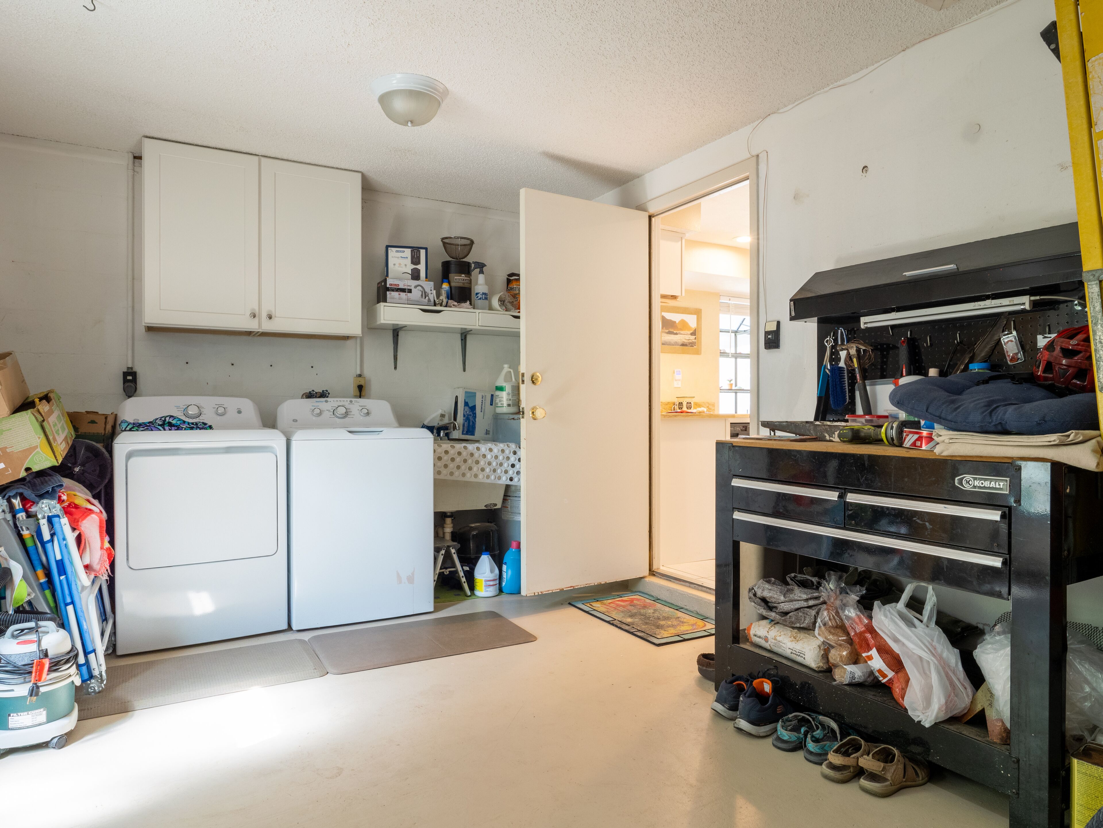 A laundry area with two washing machines, a drying rack, and a storage cabinet.