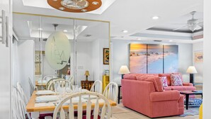 A modern living room with a dining area, featuring a red sofa, white chairs, and a dining table set for four.