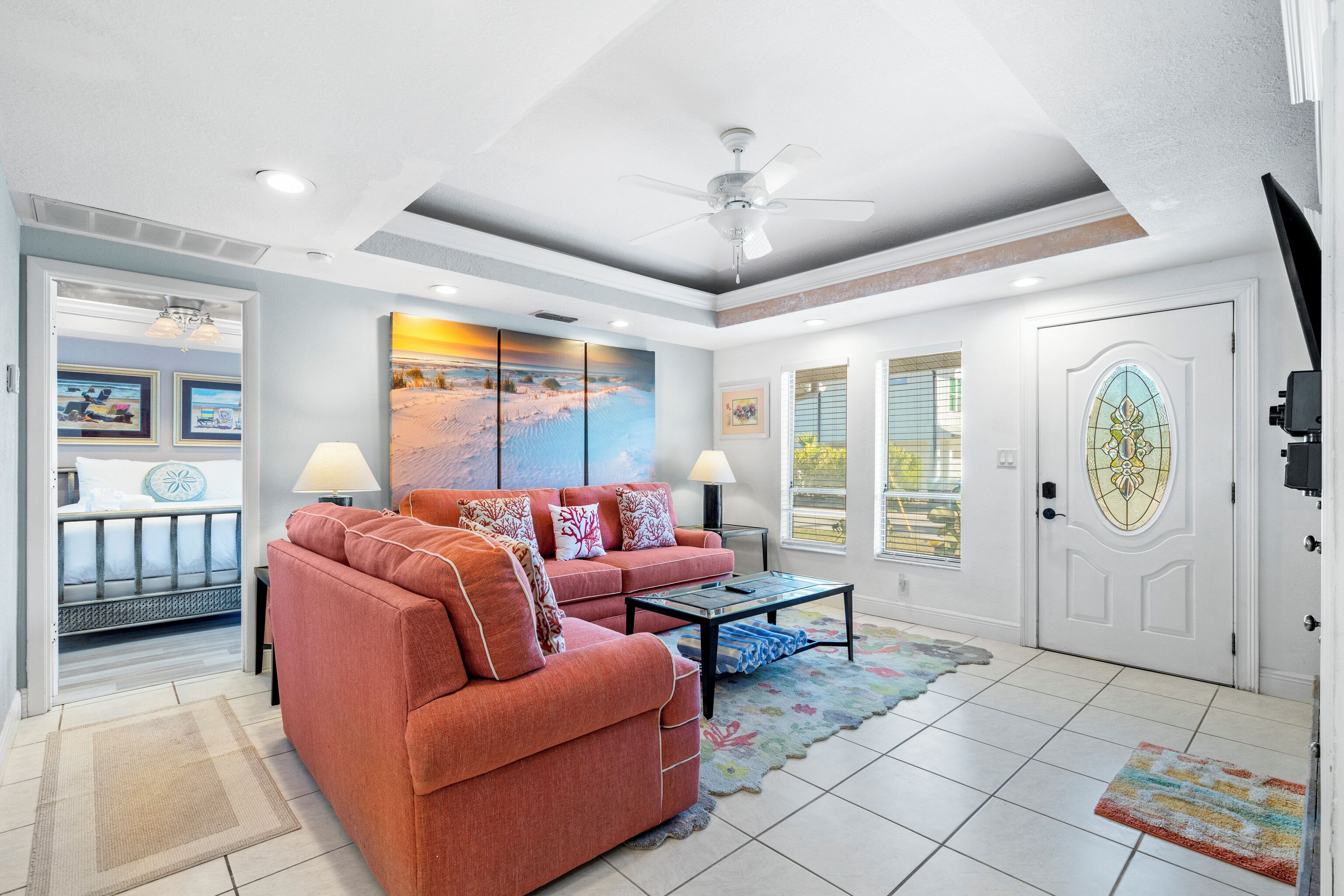 A spacious living room with a large sofa, a coffee table, and a ceiling fan. There is a door with a stained glass window and a painting on the wall.