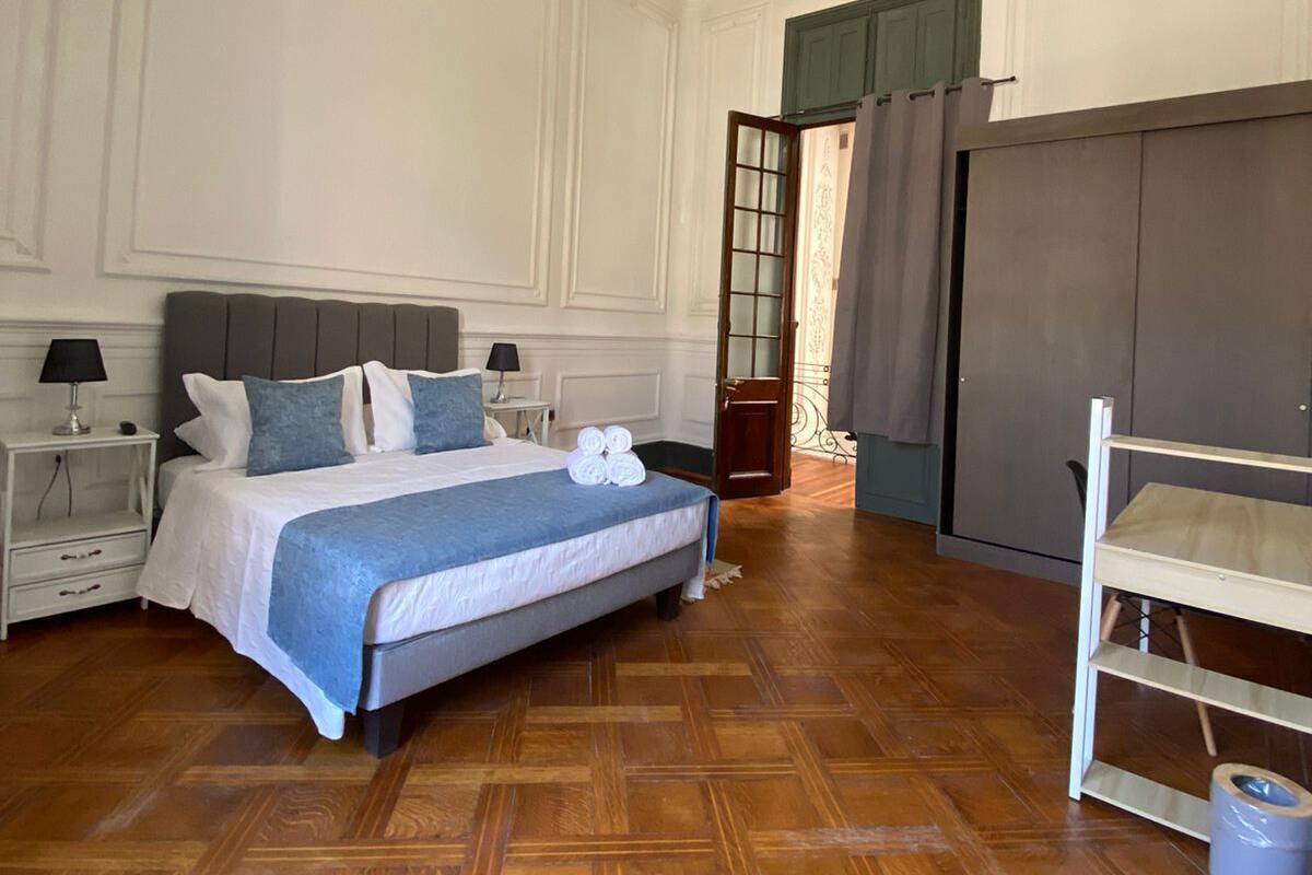 Un dormitorio con una cama grande, dos mesitas de noche, un armario y suelo de parqué de madera.