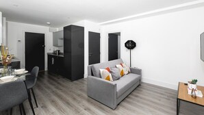 A modern living room with a grey sofa, a dining table with chairs, and a kitchen area in the background.