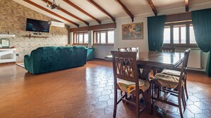 Een eethoek met een houten tafel en stoelen, een groene bank en een bakstenen muur met een televisie.