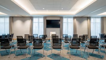 Un salón de conferencias con filas de sillas, una pantalla grande y piso alfombrado.