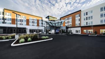 A modern hotel with a covered entrance, a parking area, and a clear sky.