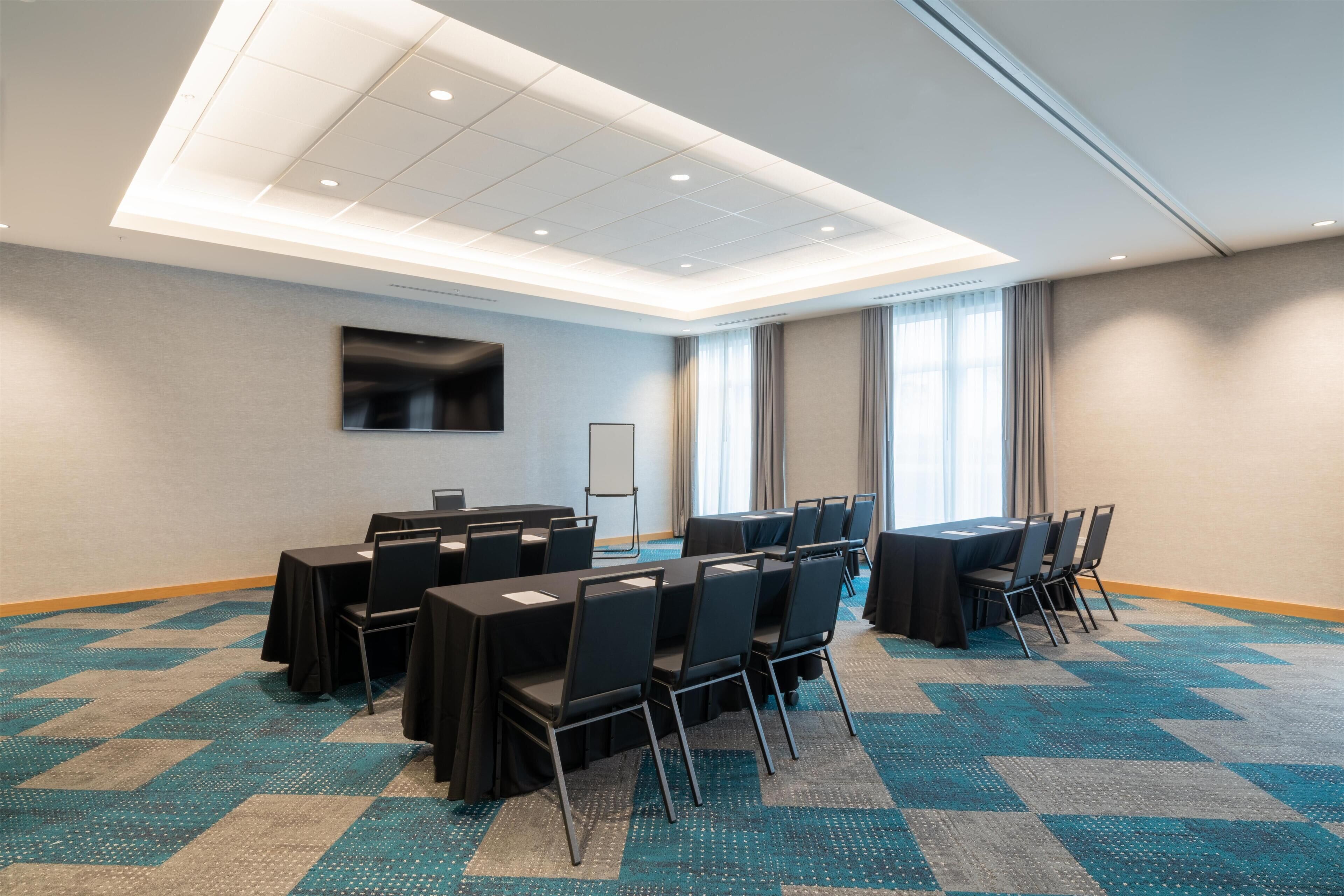 A conference room with tables and chairs, a flat-screen TV, and a large window with curtains.