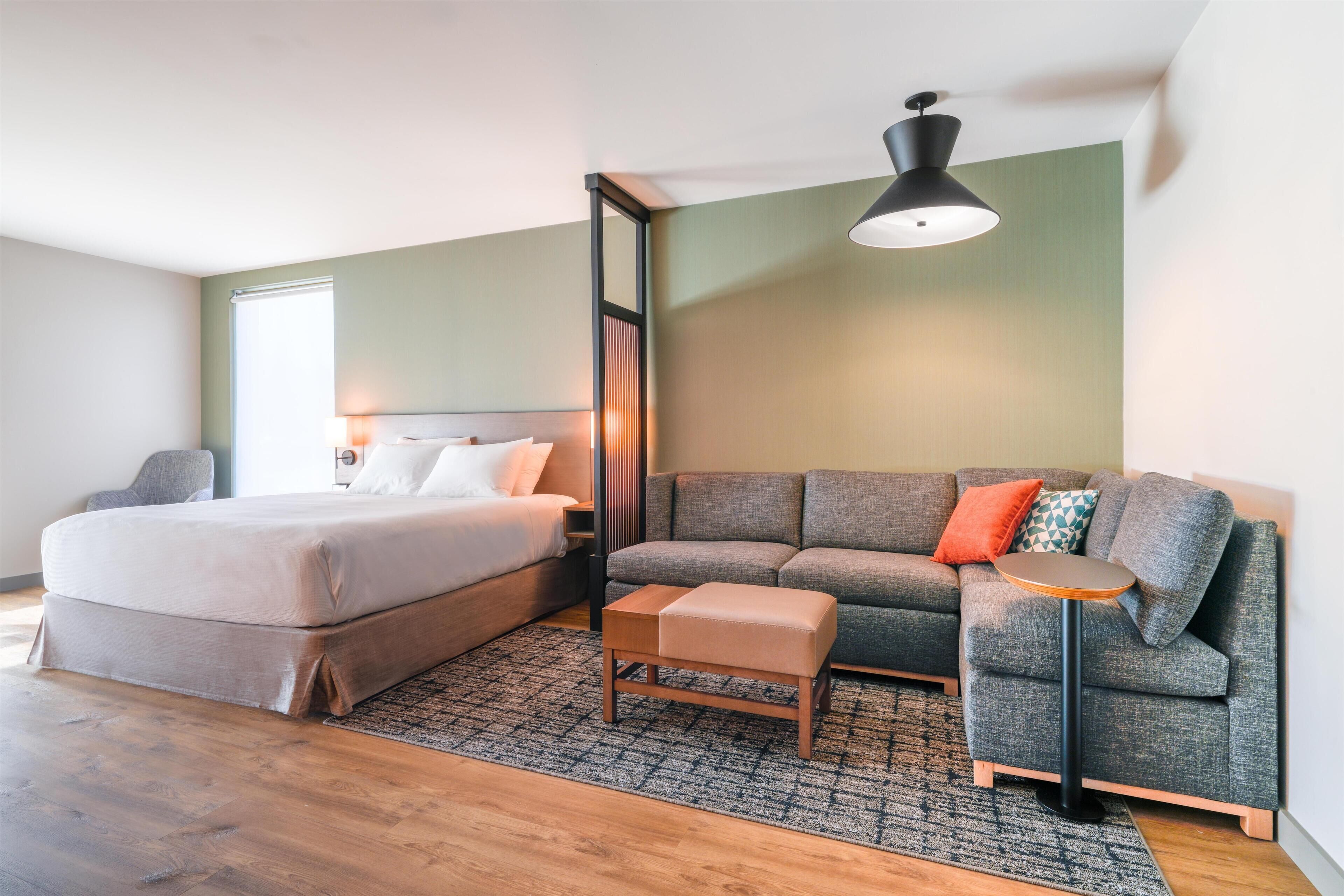 Un dormitorio moderno con cama, sofá, una mesita y una lámpara colgante.