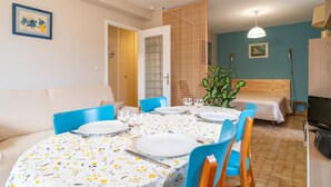 A dining area with a round table set for four, blue chairs, and a wooden headboard bed in the background.