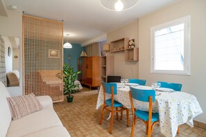 Uma sala de estar acolhedora com sofá, mesa de jantar com cadeiras, aparador de madeira e uma janela grande.