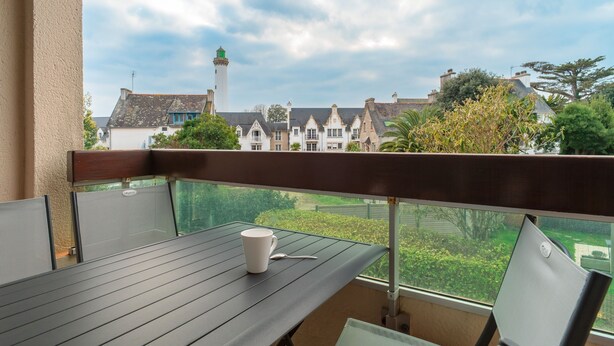 A balcony with a table and chairs, overlooking a row of houses and a lighthouse.