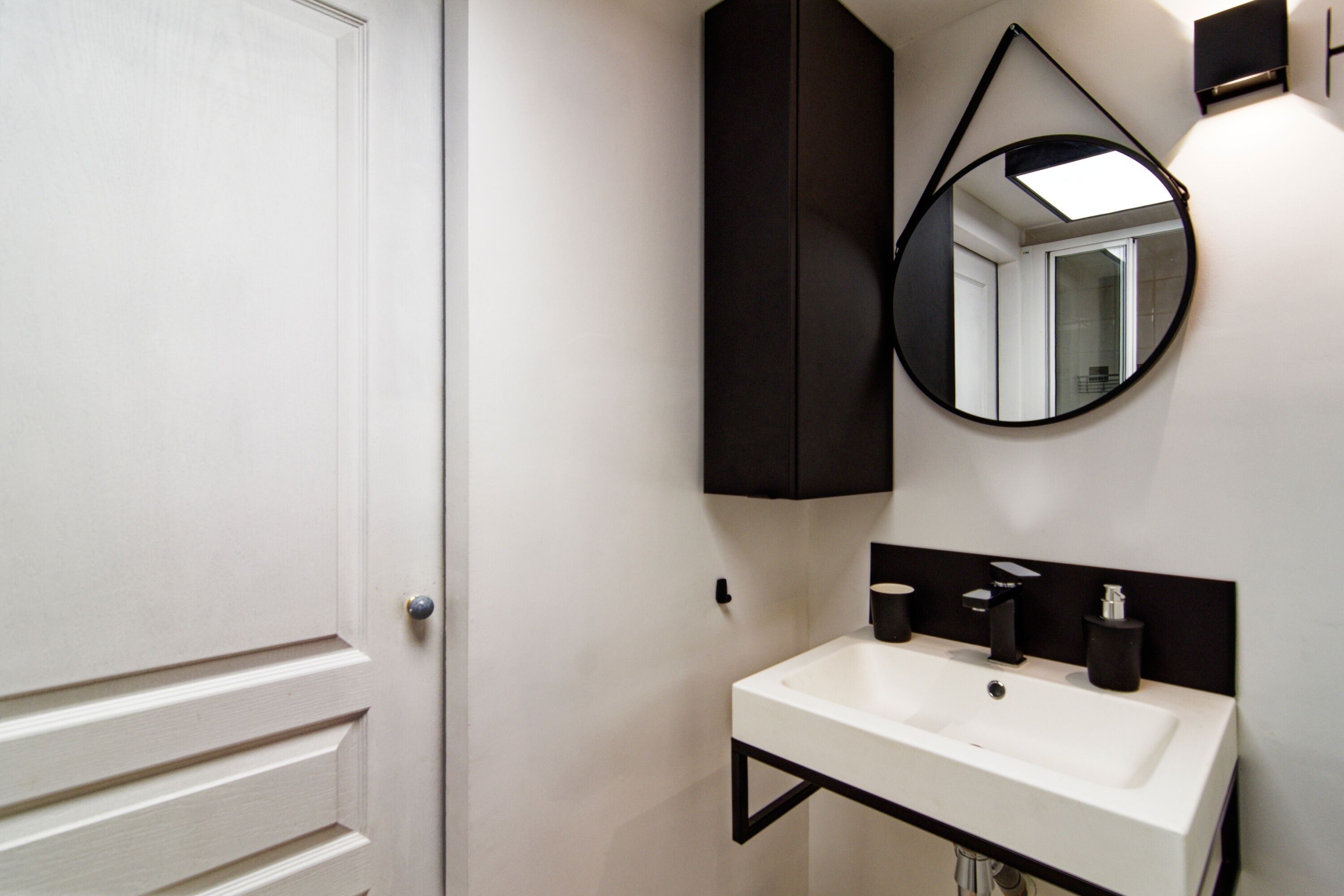 Un baño moderno con un lavabo blanco, un mueble negro y un espejo redondo.