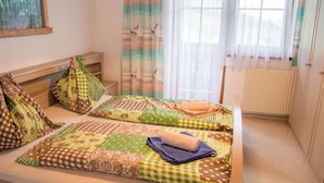 A bedroom with two beds, each with patterned bedding and pillows, a wooden headboard, a radiator, and a window with sheer curtains. - Apartment in Mittersill near KitzSki Lift (Mittersill)