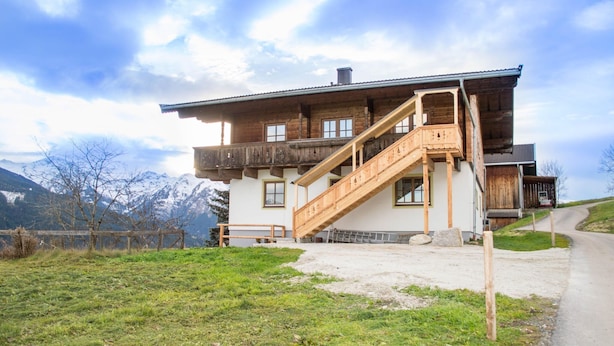 A wooden chalet with a wooden staircase leading to a balcony, surrounded by a grassy area and a dirt path. - Apartment in Mittersill near KitzSki Lift (Mittersill)
