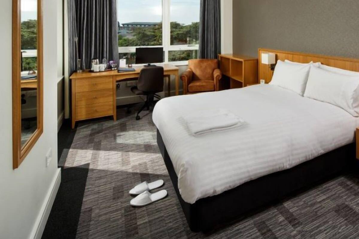Une chambre d’hôtel avec un grand lit, un bureau, une chaise, un ordinateur et une vue sur l’extérieur.