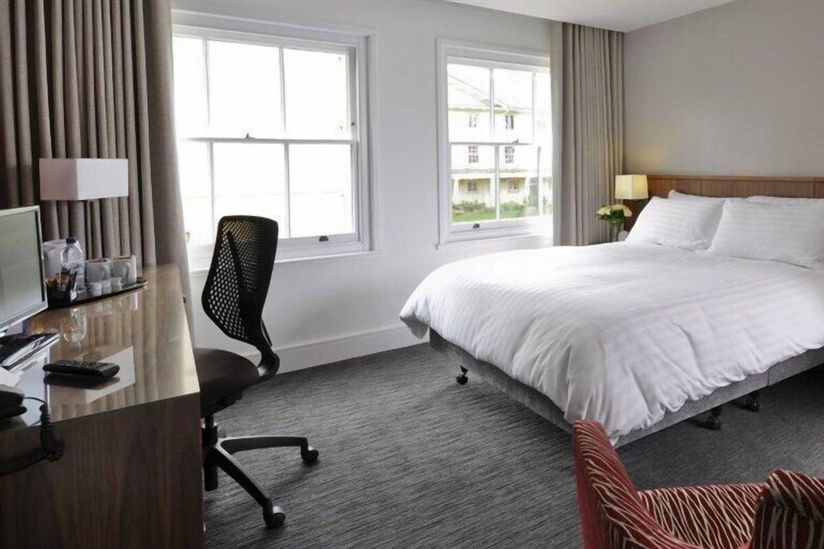 Une chambre d’hôtel avec un grand lit, un bureau avec un ordinateur, une chaise et deux lampes.