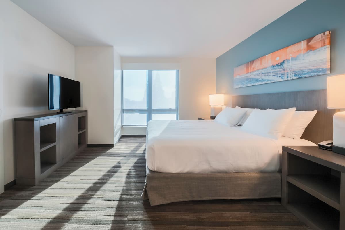 A hotel room with a bed, a TV, a desk, and a window.