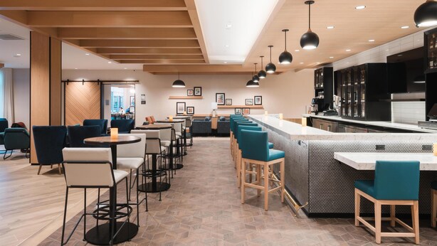 A modern restaurant with a bar area, multiple seating options, and a kitchen in the background. - Hyatt House Sacramento Airport - Natomas (Sacramento)