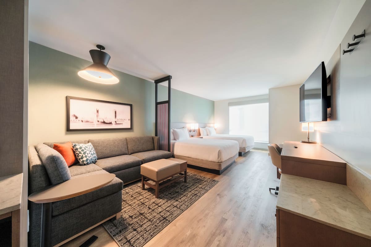 A modern hotel room with a sofa, a bed, a desk, and a television.