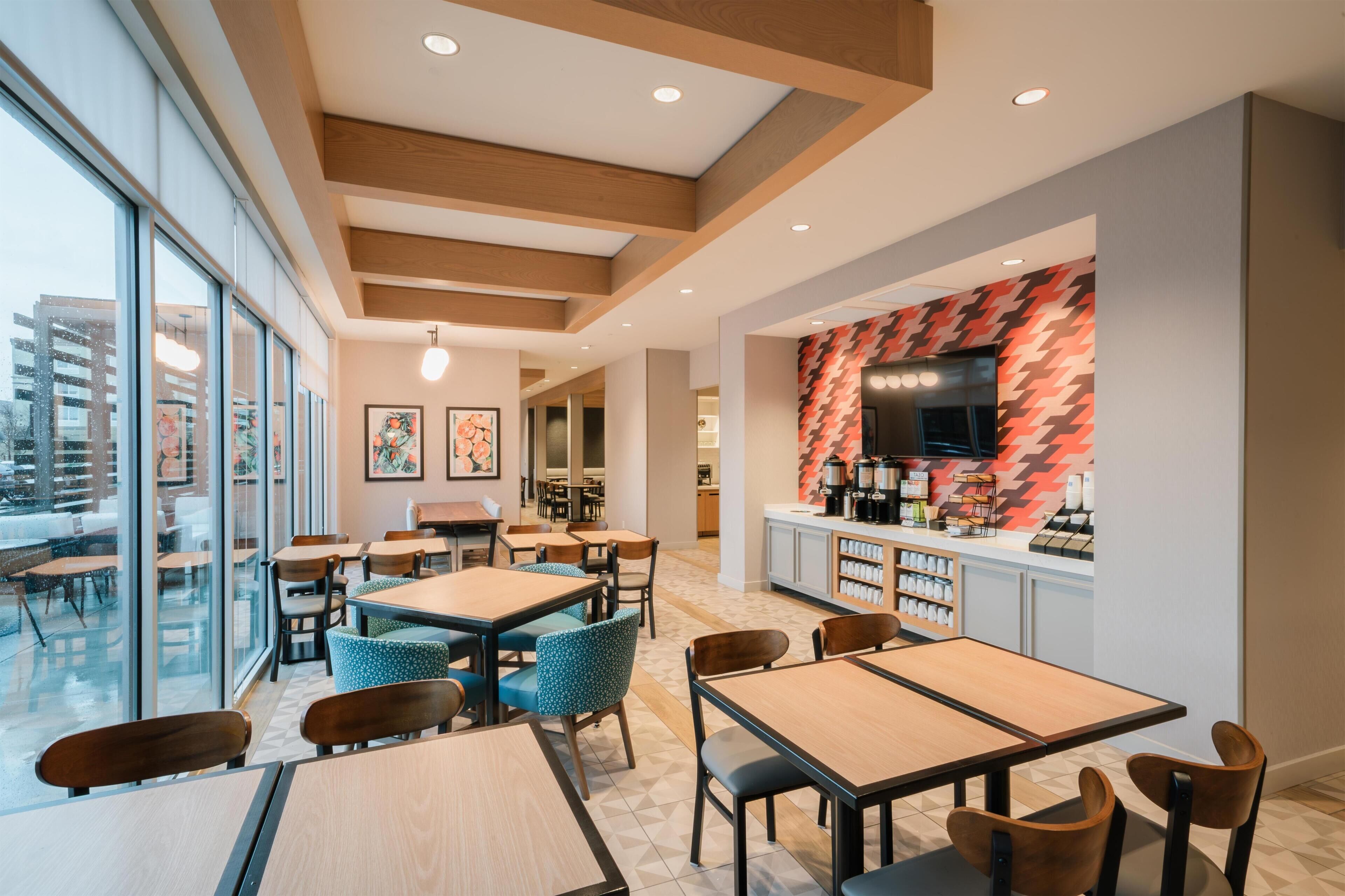 Una cafetería moderna con mesas de madera, sillas azules y una pared con motivo de espiga.