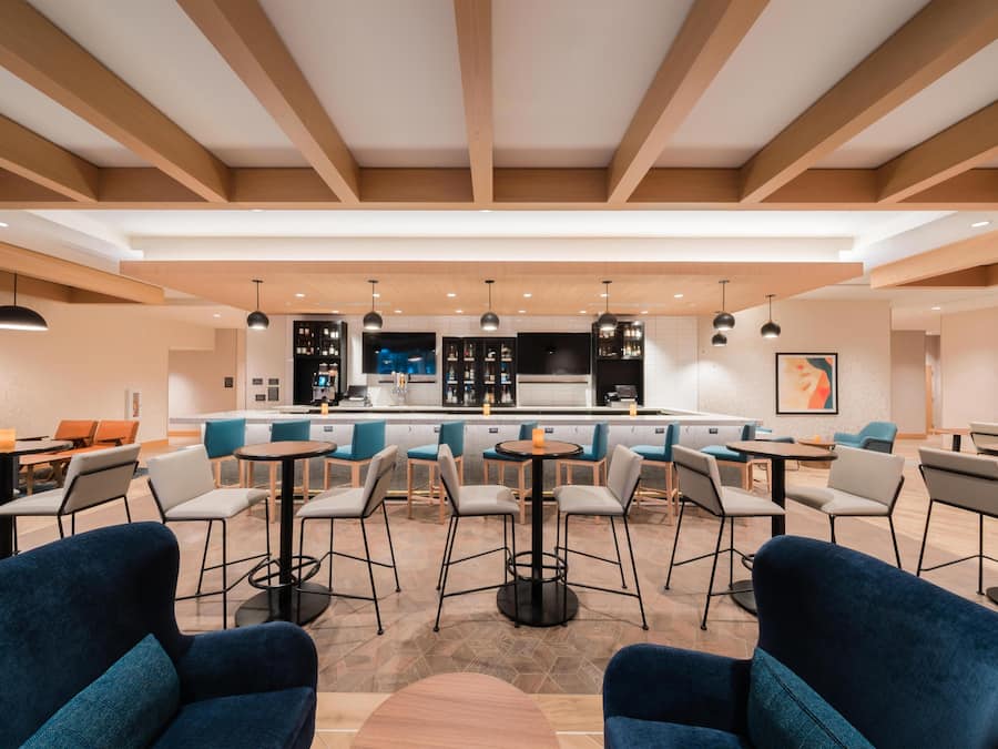 Eine moderne Hotelhalle mit Barbereich, Sitzgelegenheiten und einer Küche im Hintergrund.