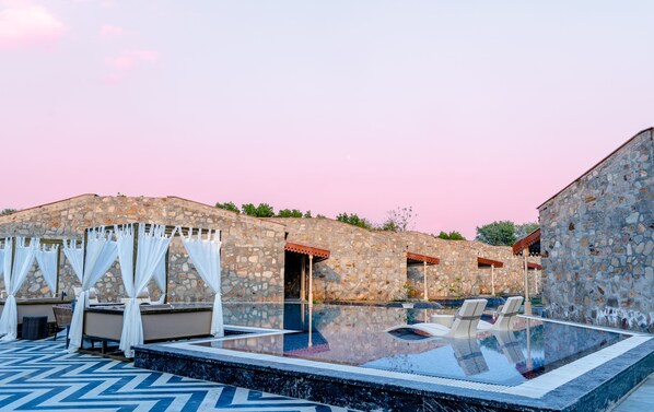 A stone building with a pool area, including lounge chairs and a covered seating area. - Brij Bageecha Jaipur - Private Villas with Heated Plunge Pool (Jamwa Ramgarh)