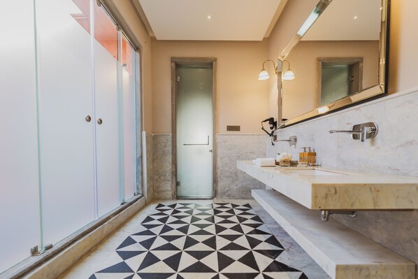 Un baño moderno con piso de diseño geométrico, cabina de ducha de vidrio y tocador con espejo e iluminación.