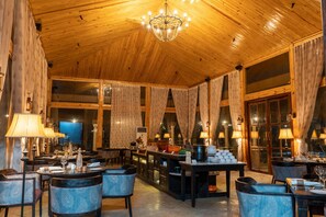 A spacious dining area with wooden ceiling and large windows, featuring tables and chairs, and a chandelier. - Brij Bageecha Jaipur - Private Villas with Heated Plunge Pool (Jamwa Ramgarh)