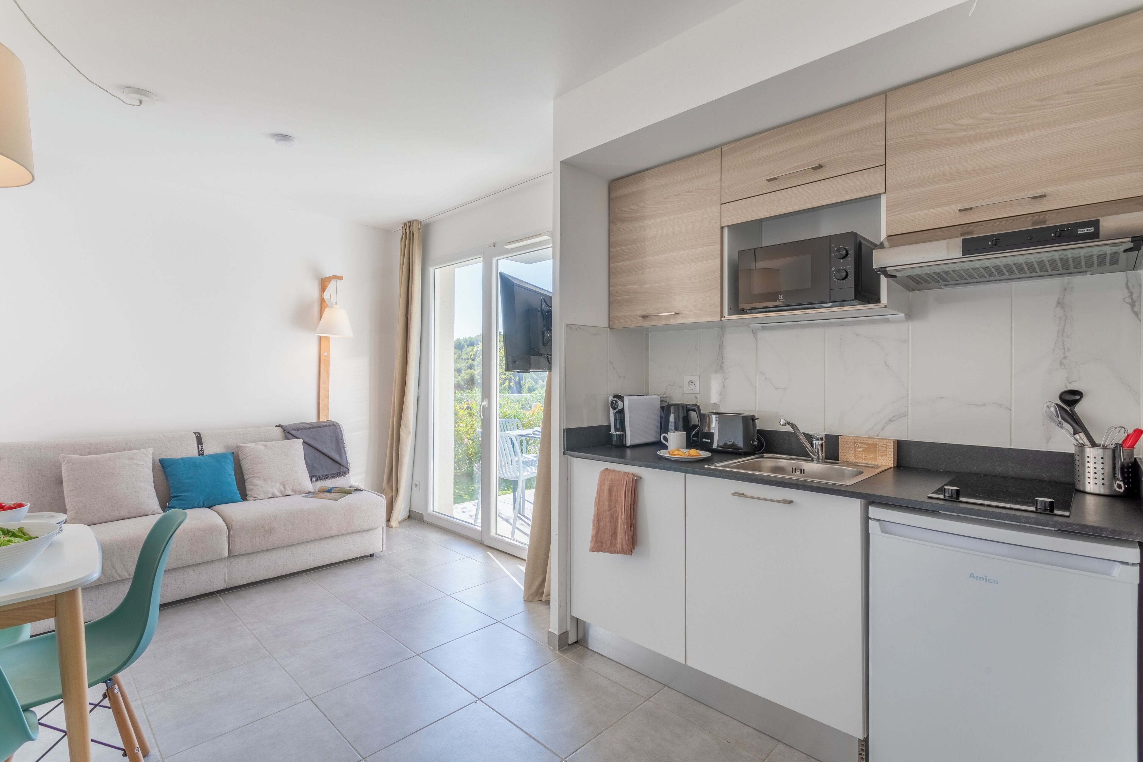 A modern kitchen with a dining area, large windows, and a view of greenery.