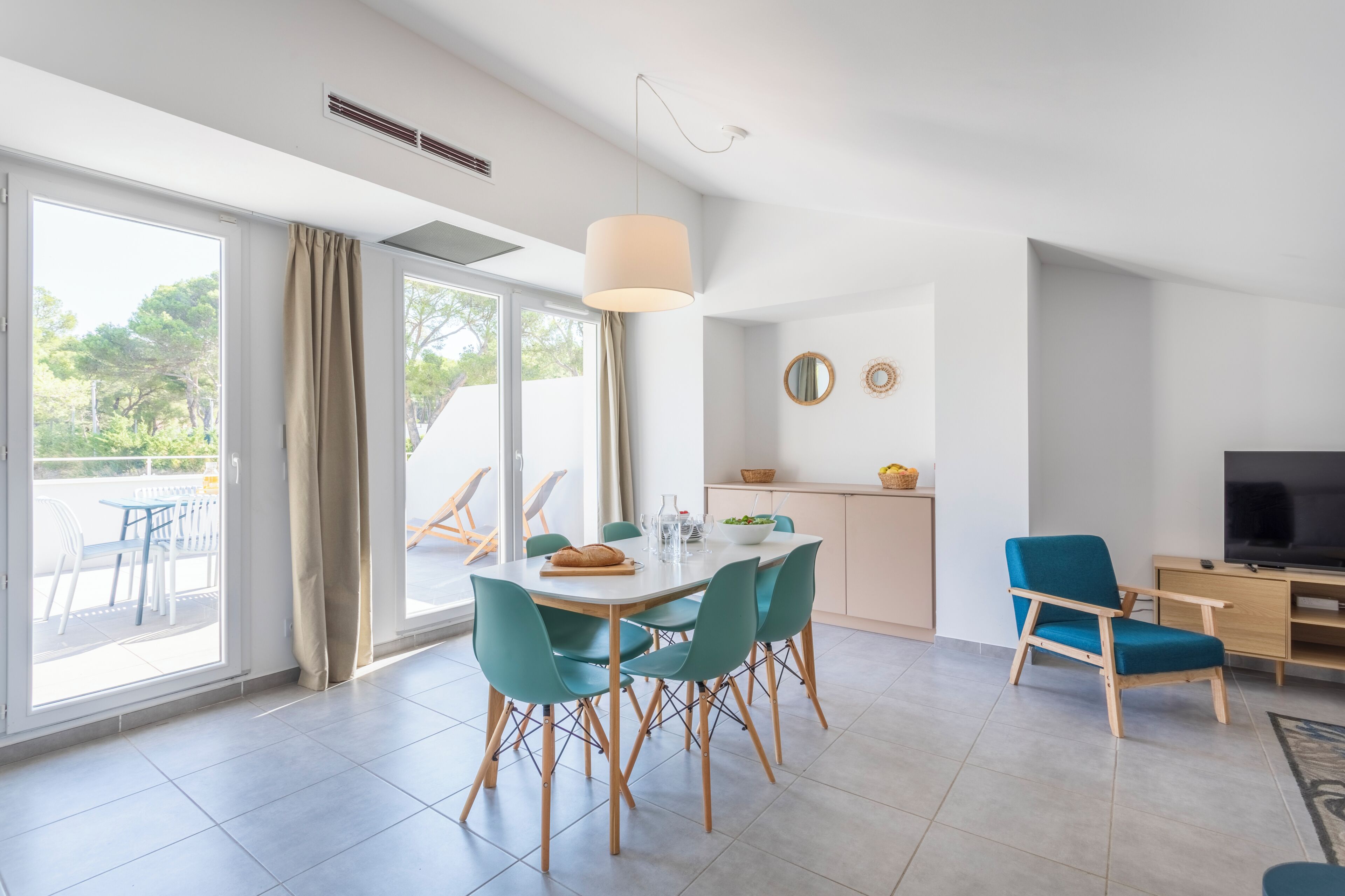 A modern living room with a dining area, a TV, and a view of the outdoors.