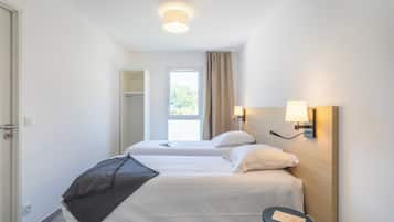 Une chambre d’hôtel avec deux lits, une petite table, une fenêtre avec des rideaux et une lampe fixée au mur.