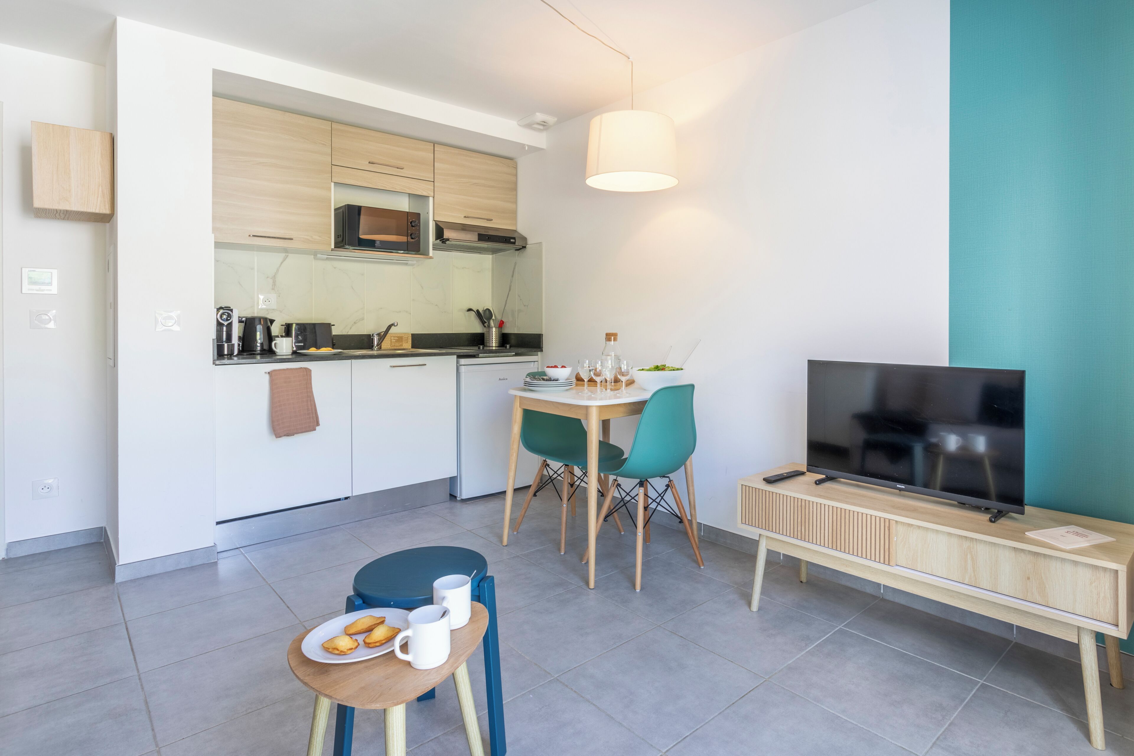 A modern kitchen with a microwave, stove, and coffee maker, a dining area with a table and chairs, and a TV on a wooden stand.