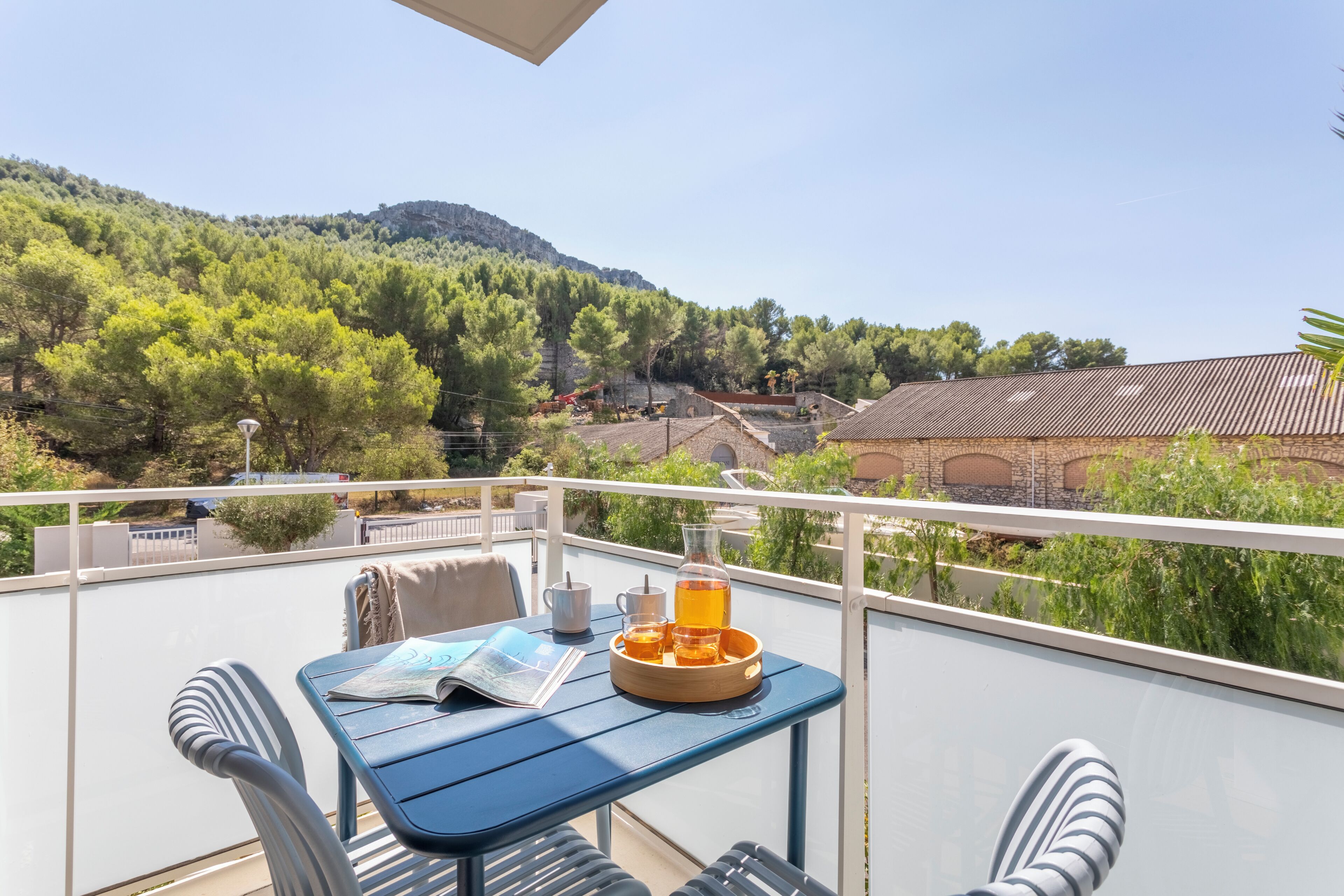 Un balcon avec une table, des chaises, un journal et un plateau avec des boissons.