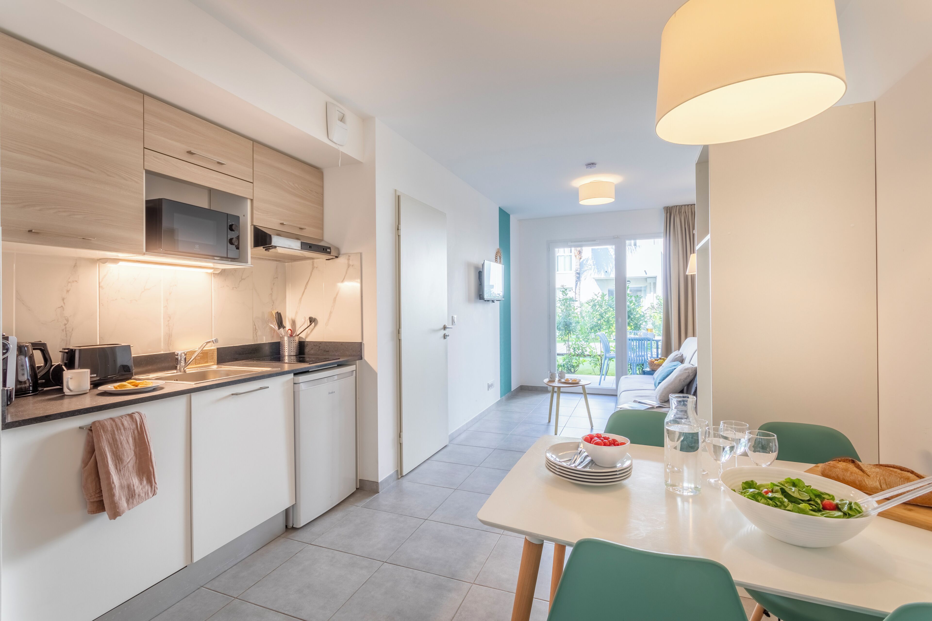 A modern kitchen with built-in appliances, a dining area with a table set for two, and a view of the outdoors.