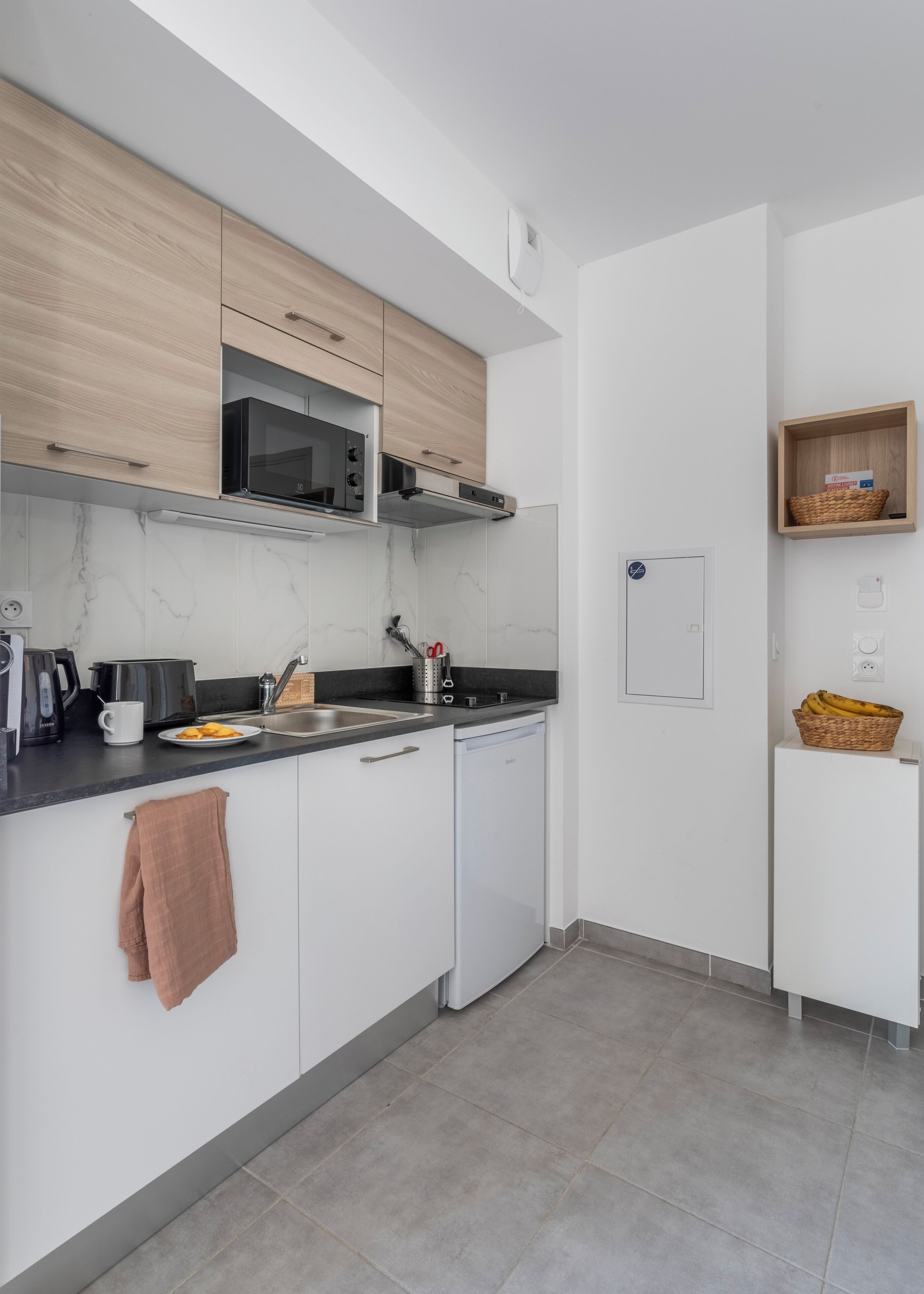 A modern kitchen with white cabinets, a microwave, a dishwasher, and a small shelf with a basket.