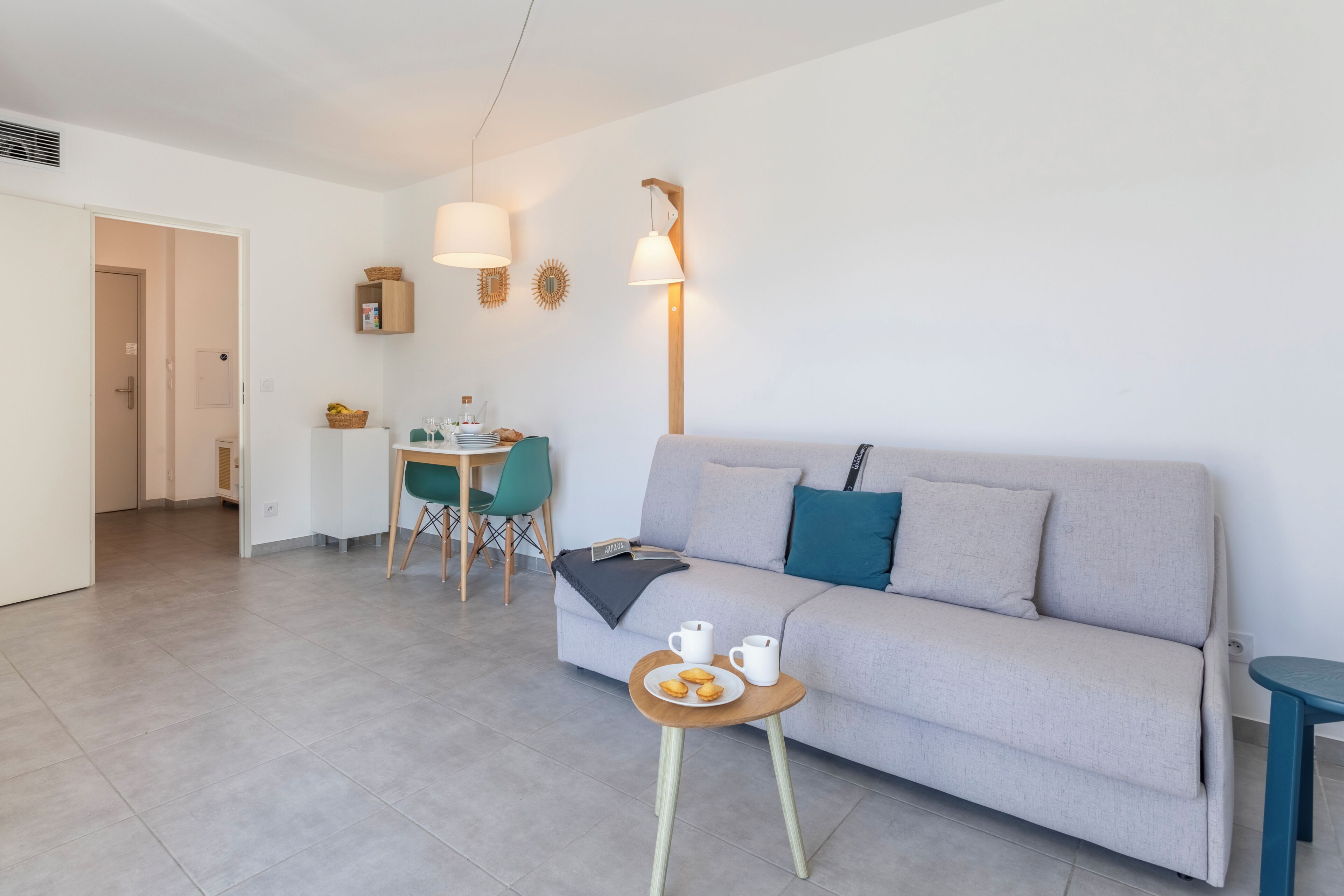 Ein modernes Wohnzimmer mit einer Couch, einem kleinen Tisch mit Getränken, einem Essbereich mit Stühlen und einer Lampe.