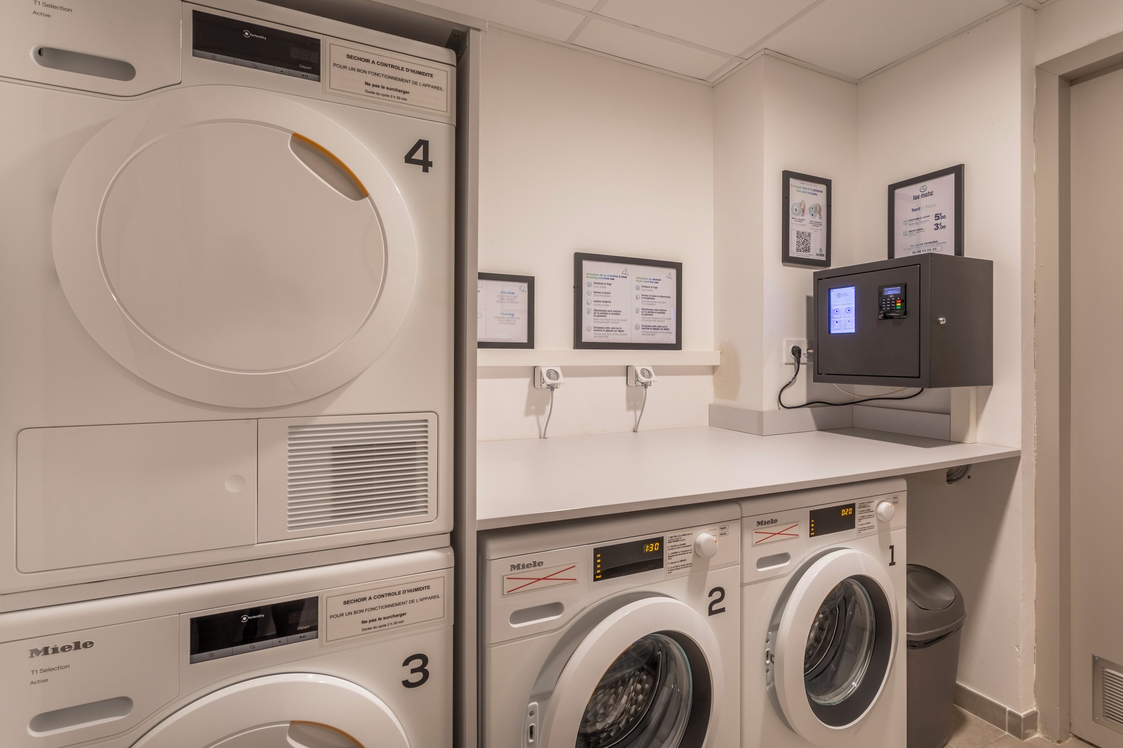 A laundry area with four washing machines, numbered 1 to 4, and a control panel above.