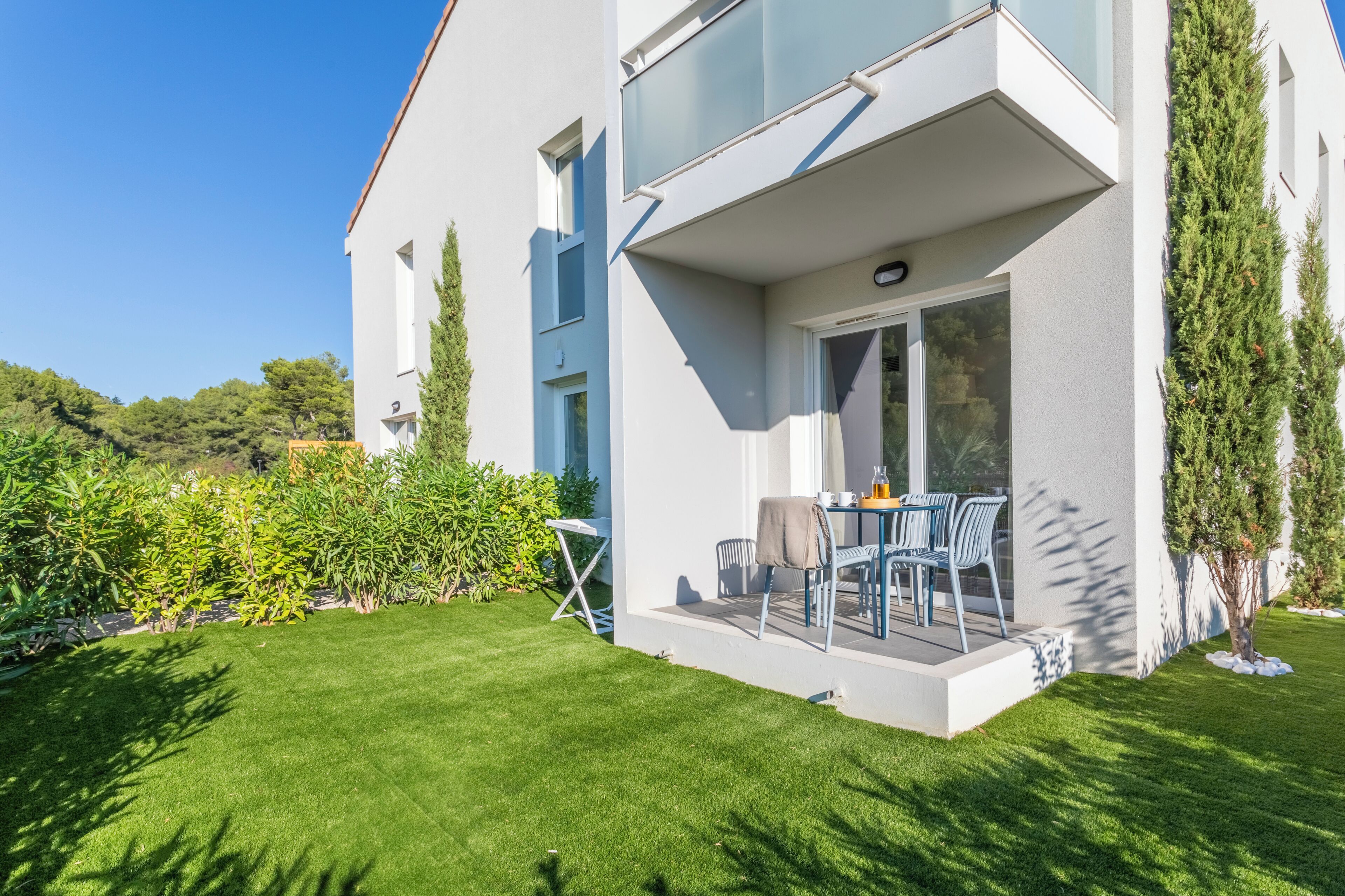 A modern two-story house with a balcony, a well-maintained lawn, and a variety of plants.