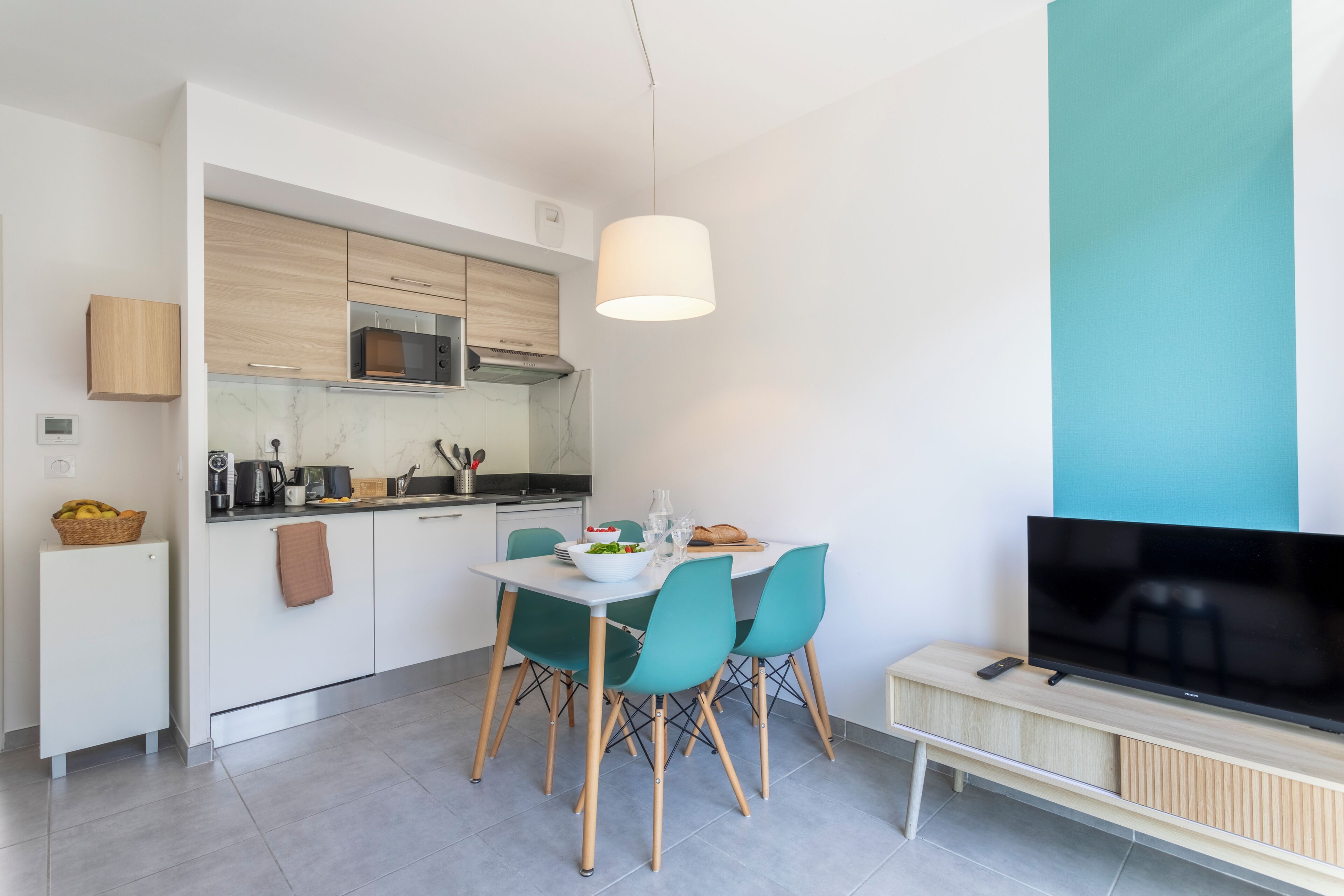 A modern kitchen with white cabinets, a microwave, and a dining area with teal chairs and a white table.