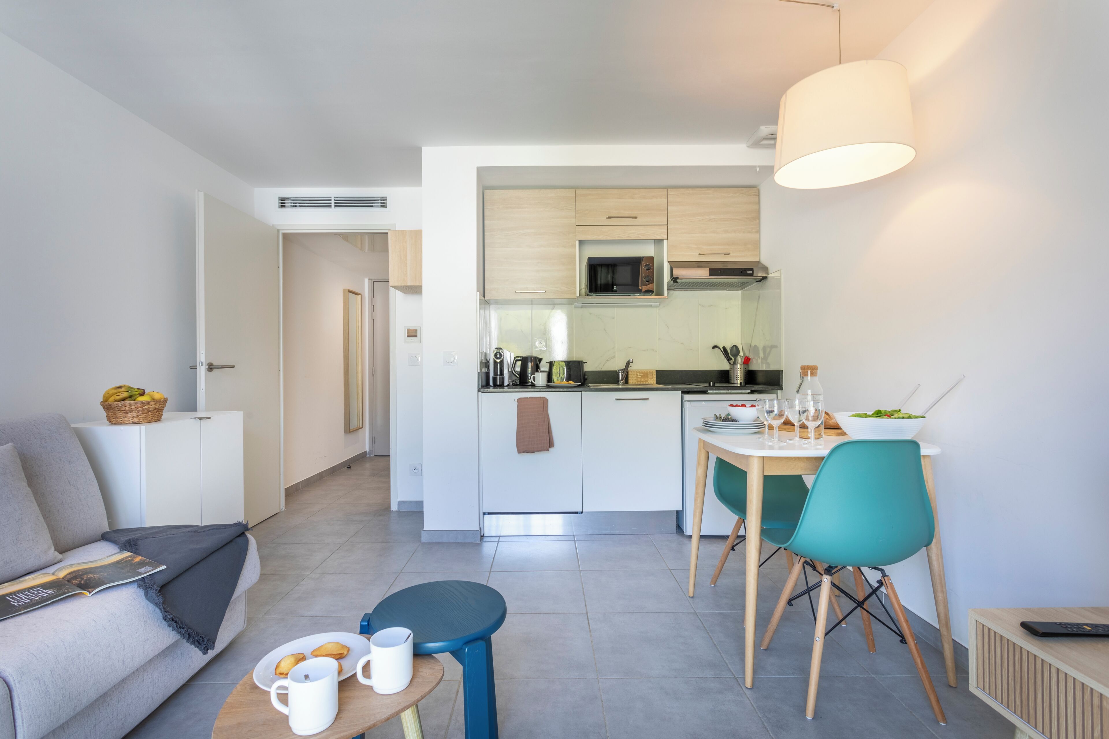 Une cuisine moderne avec des meubles blancs, un four à micro-ondes et un coin repas comprenant des chaises et une table de couleur turquoise.