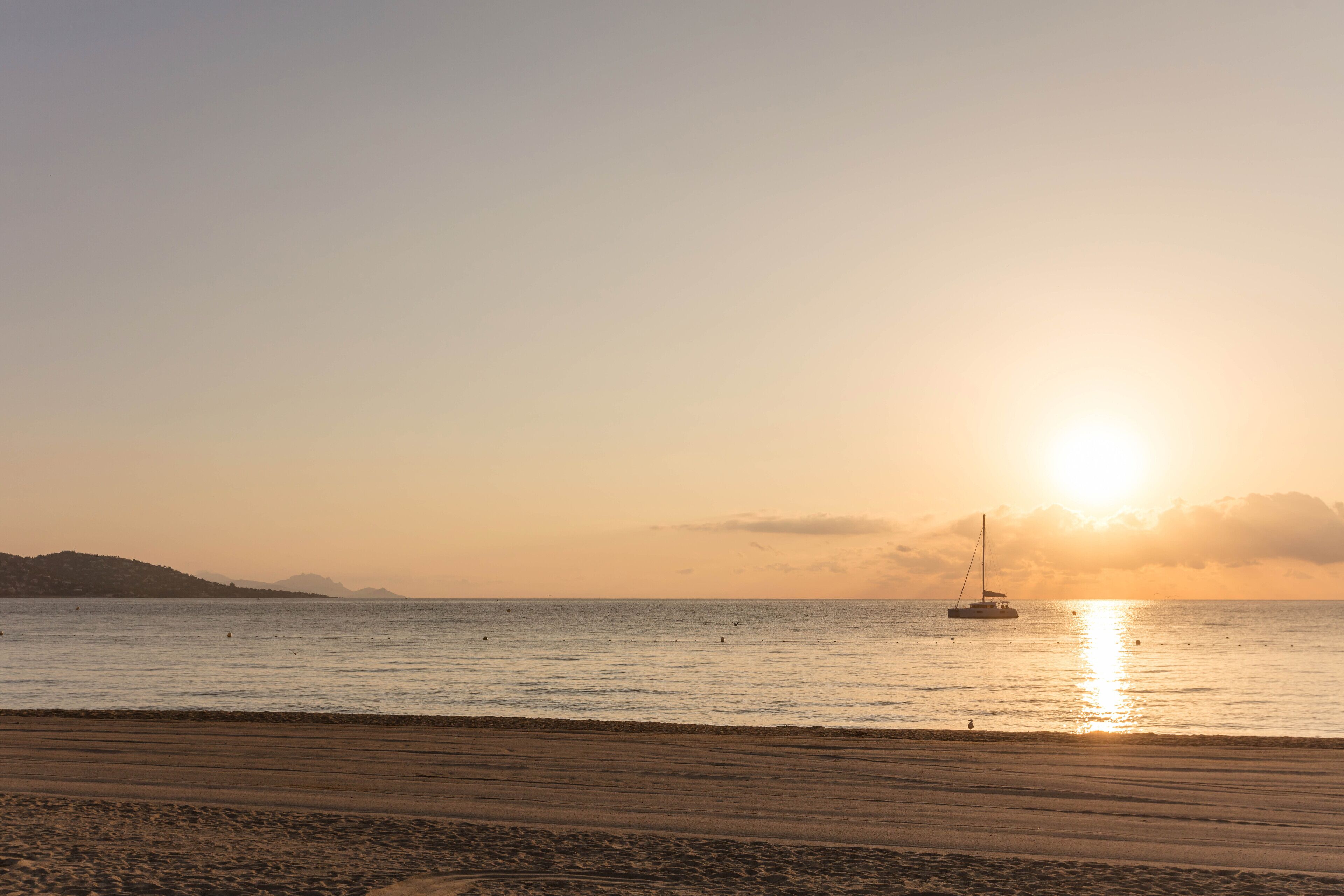 Une plage avec un voilier, une mer calme et un coucher de soleil.