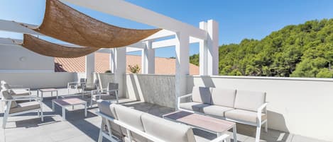 A rooftop patio with outdoor seating, a pergola, and a view of a forested hill.