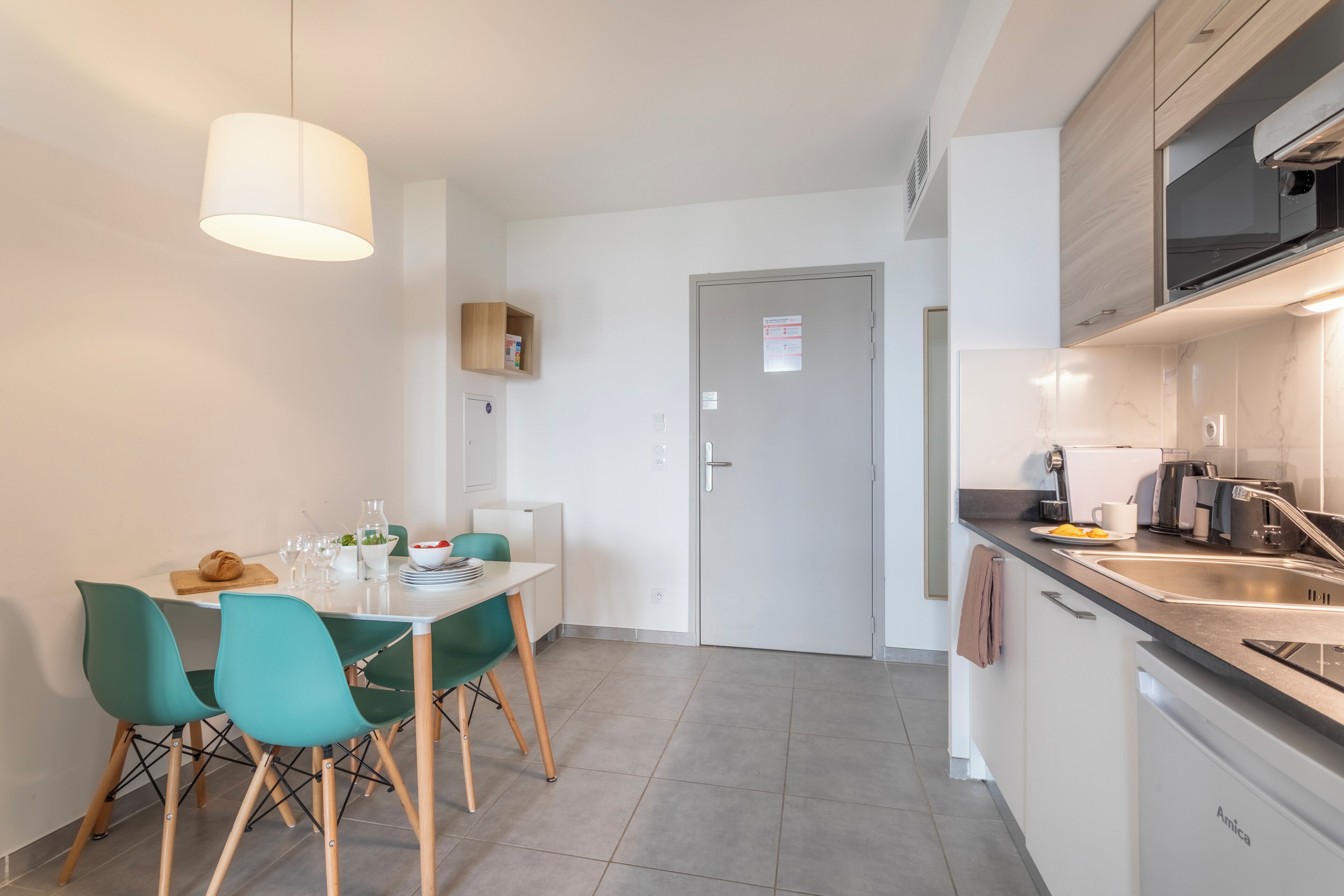 Een moderne keuken met een eethoek, met een witte tafel, groene stoelen en een hangende lamp.