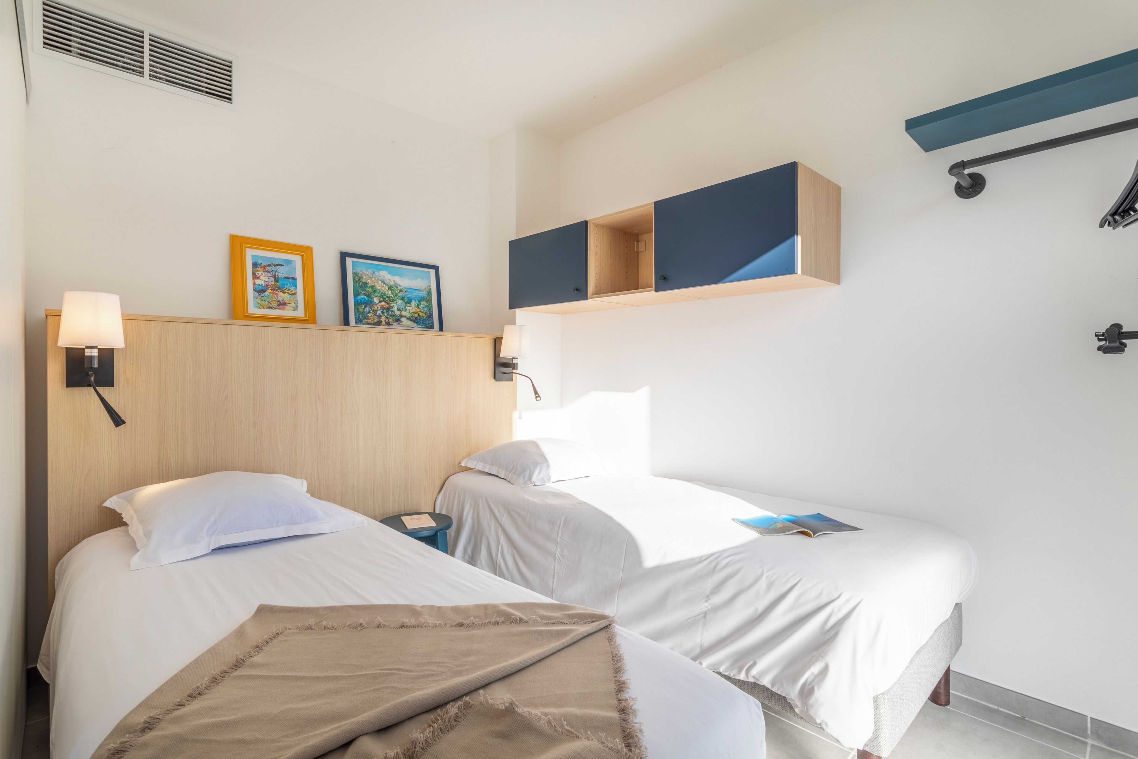 Ein Hotelzimmer mit zwei Betten, einem Holzkopfende, Wandregalen und einem Deckenlüfter.