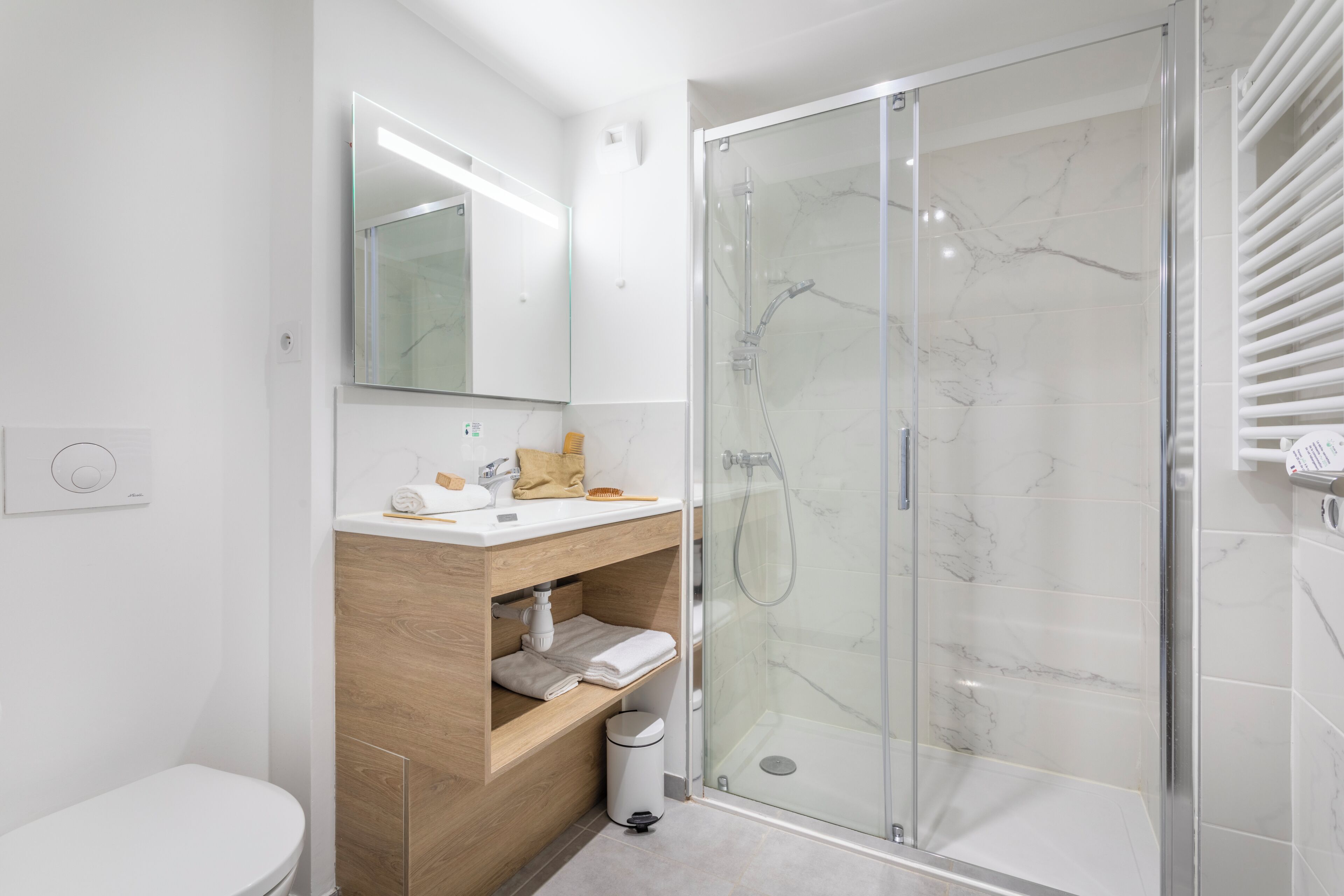 A modern bathroom with a glass-enclosed shower, a wooden vanity, and a white toilet.