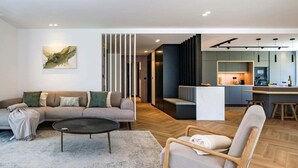 Un salon moderne avec un canapé, une table basse et un fauteuil. On y trouve également un coin cuisine avec des placards et une table à manger.