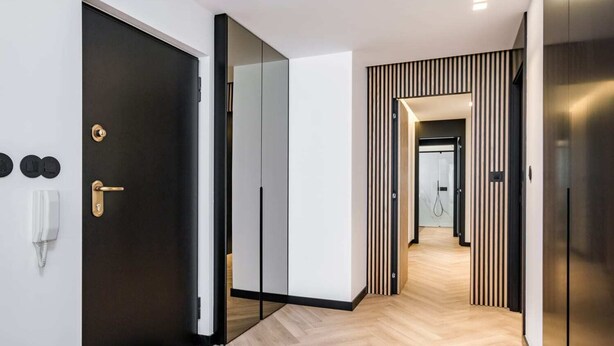 Un couloir d’hôtel moderne avec une porte noire, un téléphone et un paillasson.