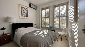A bedroom with a bed, a chair, a lamp, a picture on the wall, and a window with blinds.