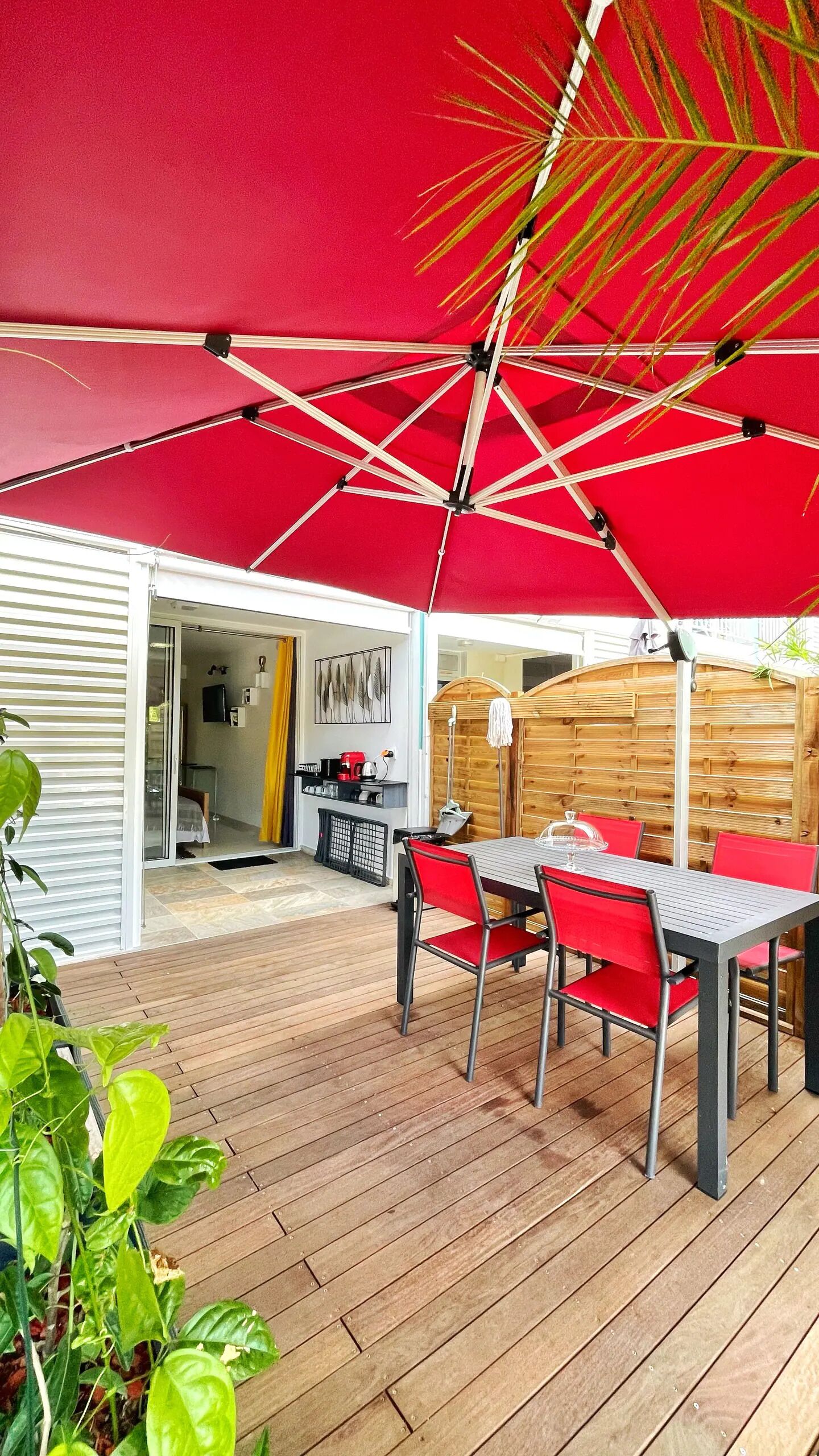 An outdoor patio with a red umbrella, wooden deck, and red chairs.
